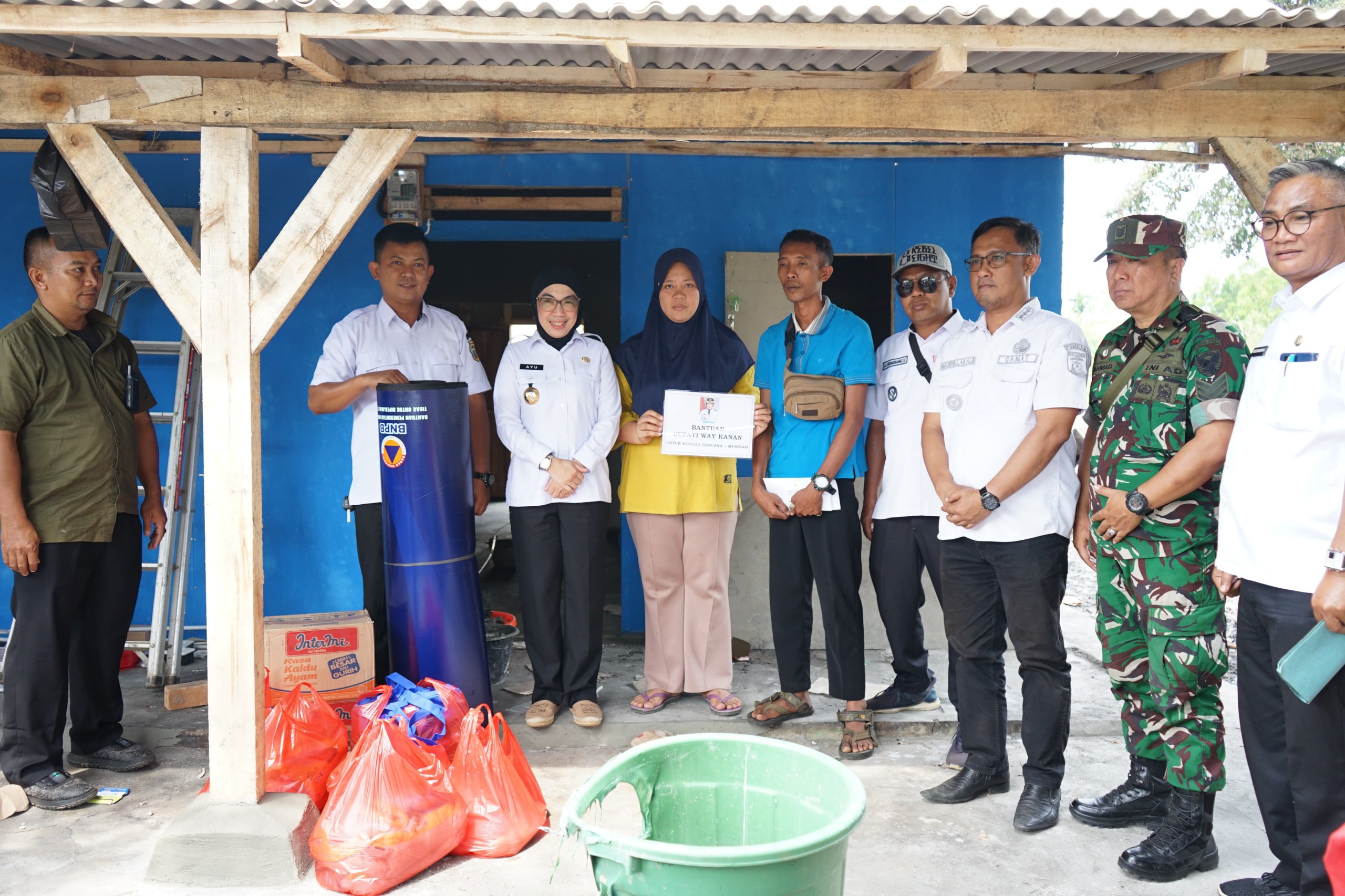 Bupati Way Kanan Ayu Asalasiyah, S. Ked., didampingi jajaran Dinas Sosial, BPBD, TNI, dan aparat Kelurahan Pasar Banjit, menyerahkan bantuan kepada keluarga korban kebakaran di Kelurahan Pasar Banjit, Kecamatan Banjit, Rabu (23/7/2025).
