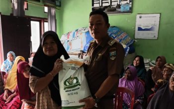 Peratin Kota Karang, Ridhoni, S.Pd., secara simbolis menyerahkan bantuan beras kepada salah satu warga penerima manfaat dalam kegiatan penyaluran bantuan pangan di Balai Pekon Kota Karang, Kecamatan Pesisir Utara, Selasa (29/7/2025).